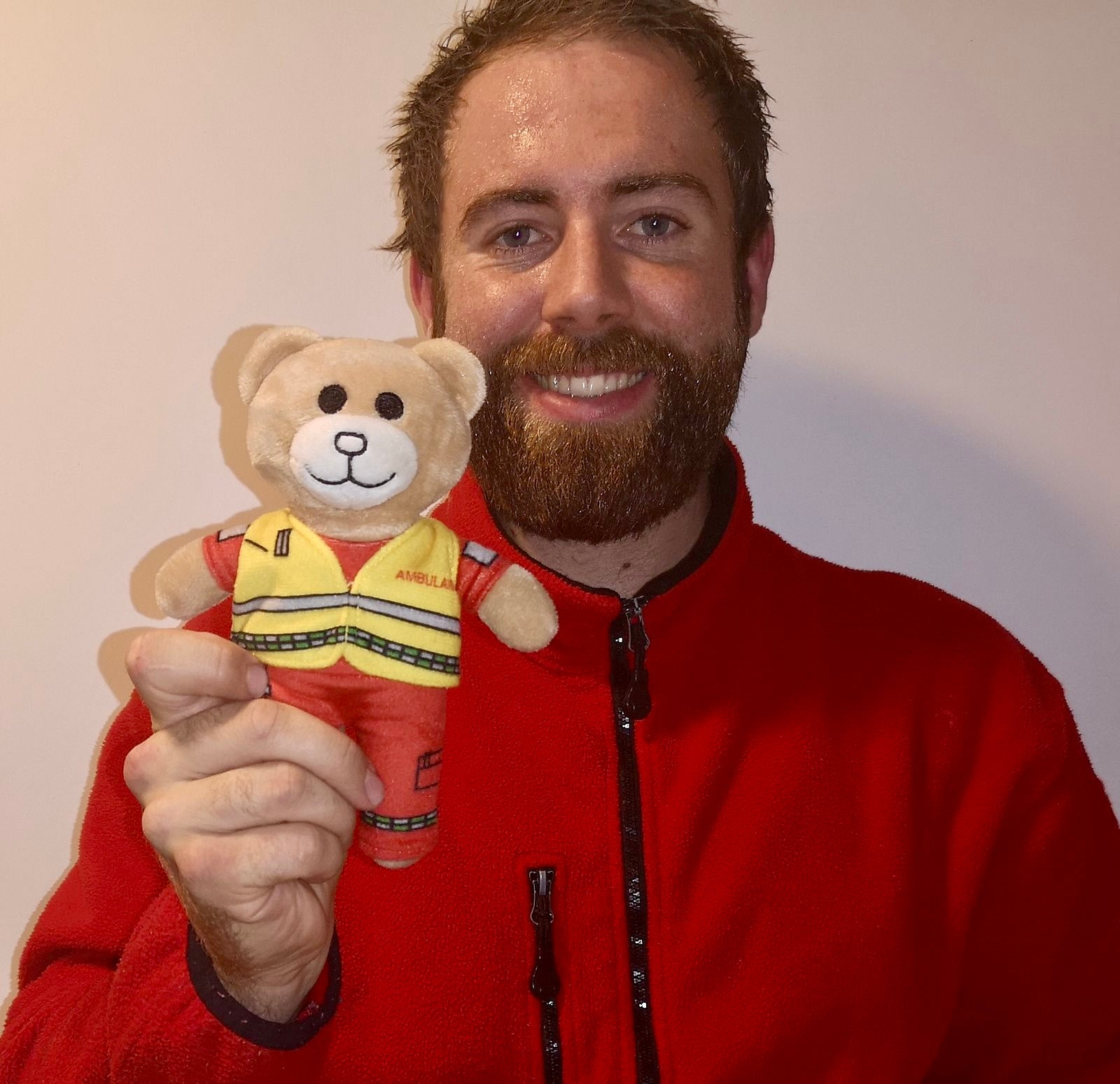 Norwegian paramedic in matching red ambulance jacket holding the Ambulansebamsen bear